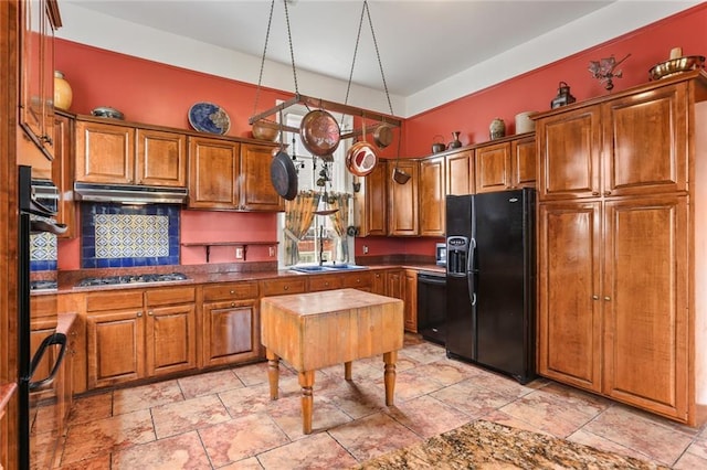 kitchen with under cabinet range hood, a sink, brown cabinets, black appliances, and dark countertops