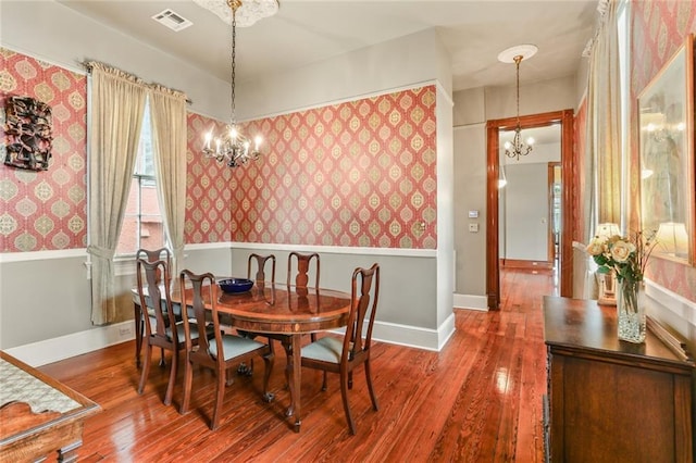 dining room featuring wallpapered walls, baseboards, visible vents, wood finished floors, and a notable chandelier