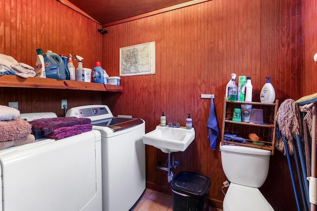 clothes washing area featuring washer and clothes dryer, wood walls, and light tile patterned flooring