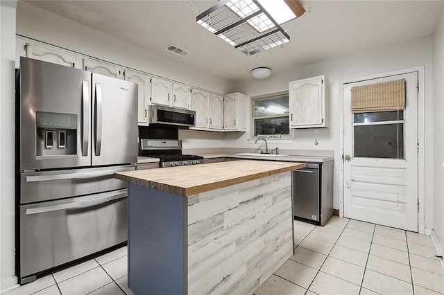 kitchen with butcher block counters, sink, light tile patterned flooring, a kitchen island, and appliances with stainless steel finishes