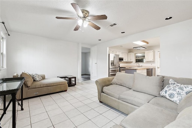 tiled living room featuring a textured ceiling, ceiling fan, wooden walls, and sink