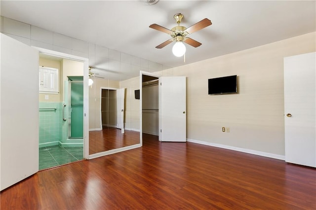 unfurnished bedroom featuring ensuite bath, ceiling fan, dark wood-type flooring, and tile walls