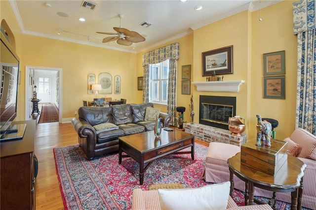 living room with ceiling fan, light hardwood / wood-style floors, crown molding, and a brick fireplace