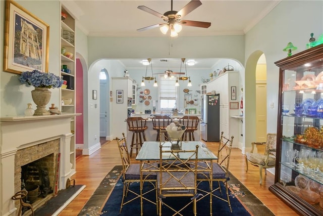 dining area with a tile fireplace, crown molding, ceiling fan, built in shelves, and light hardwood / wood-style floors