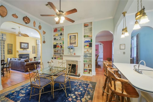 dining area with crown molding, built in features, ceiling fan, and light hardwood / wood-style floors