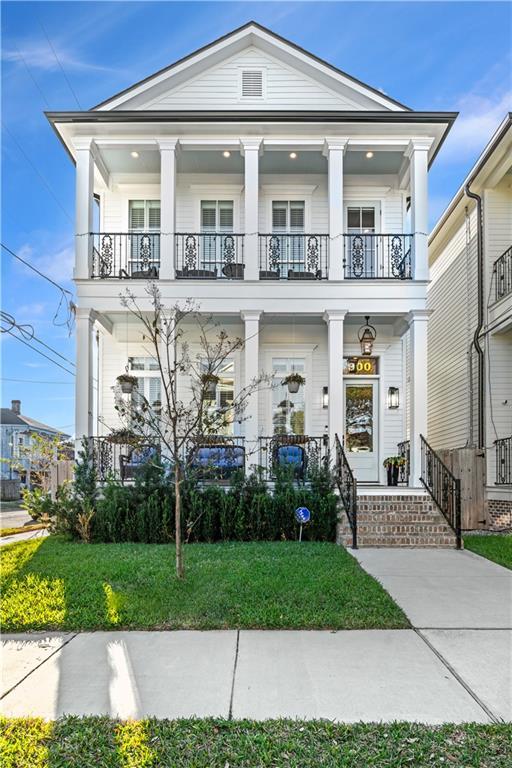 neoclassical home featuring a balcony, a front lawn, and covered porch