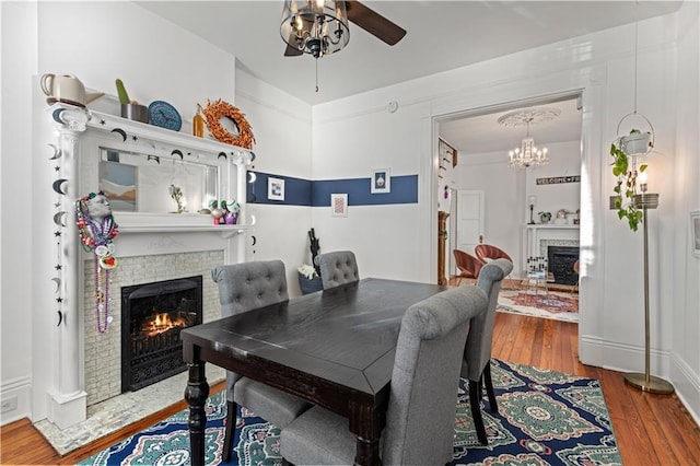 dining space with ceiling fan with notable chandelier, wood-type flooring, and a fireplace