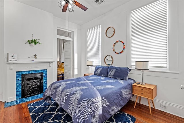 bedroom featuring a fireplace, ceiling fan, and hardwood / wood-style floors