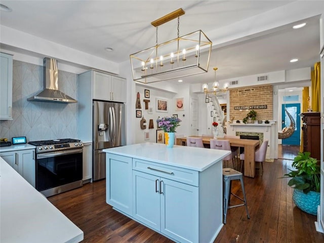 kitchen with appliances with stainless steel finishes, dark wood-type flooring, wall chimney range hood, pendant lighting, and a kitchen island