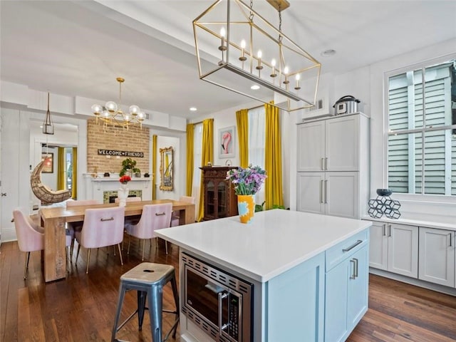 kitchen featuring stainless steel microwave, a center island, dark hardwood / wood-style flooring, a notable chandelier, and pendant lighting