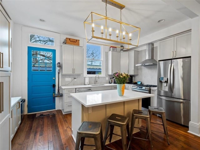 kitchen with dark wood-type flooring, sink, wall chimney exhaust hood, appliances with stainless steel finishes, and a kitchen island