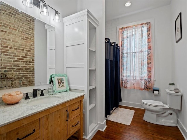 bathroom with hardwood / wood-style floors, vanity, brick wall, and toilet