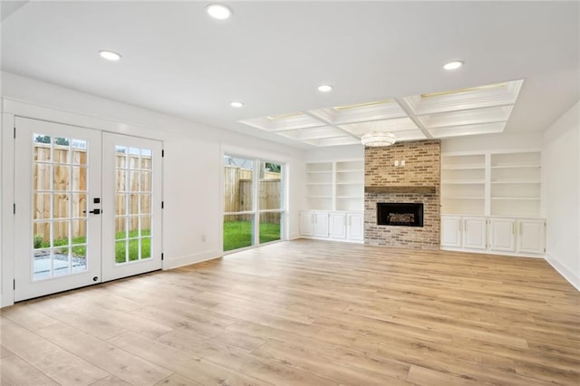 unfurnished living room featuring built in shelves, french doors, a brick fireplace, an inviting chandelier, and light wood-type flooring