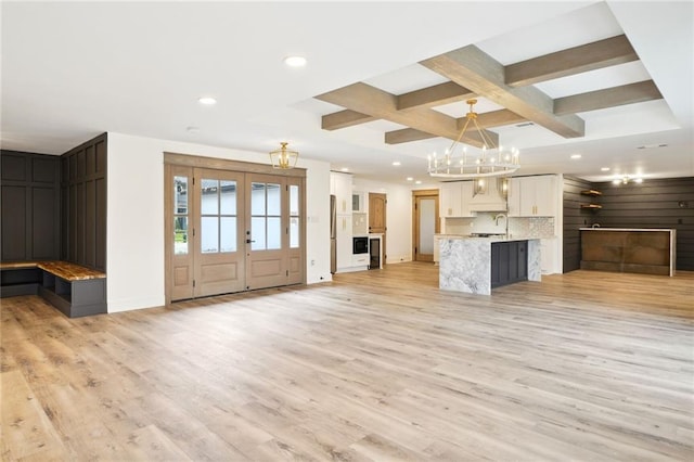 unfurnished living room featuring french doors, sink, light hardwood / wood-style flooring, beamed ceiling, and wooden walls