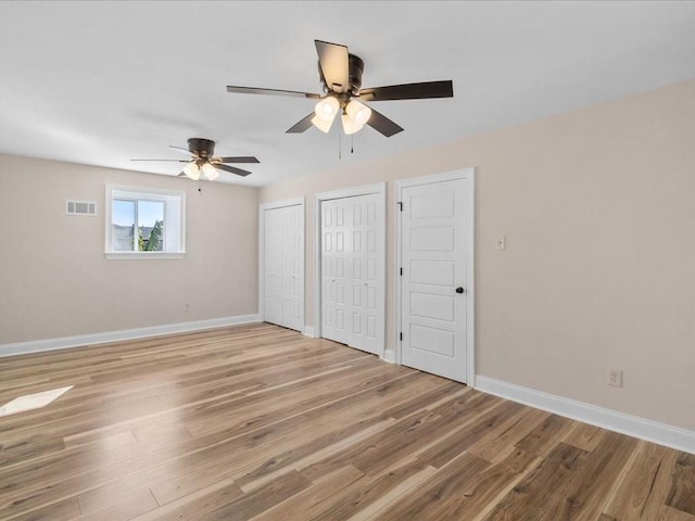 unfurnished bedroom with two closets, light hardwood / wood-style floors, and ceiling fan