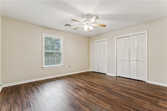 unfurnished bedroom featuring multiple closets, dark hardwood / wood-style flooring, and ceiling fan