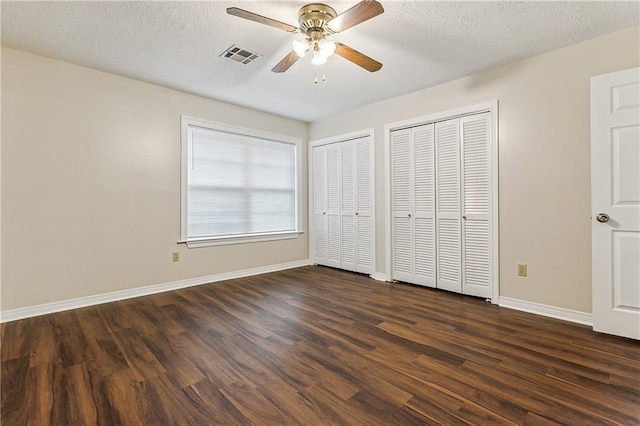 unfurnished bedroom with multiple closets, a textured ceiling, dark wood-type flooring, and ceiling fan