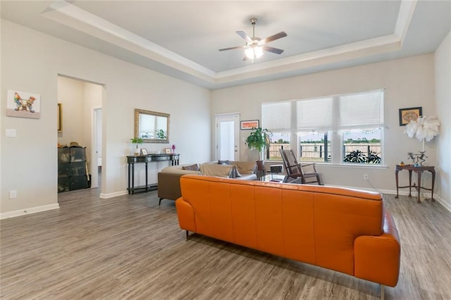 living room with a raised ceiling, ceiling fan, and wood-type flooring