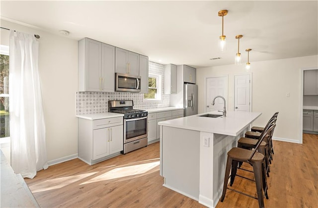 kitchen with sink, hanging light fixtures, light hardwood / wood-style flooring, gray cabinets, and stainless steel appliances