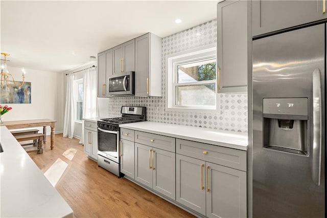 kitchen with gray cabinetry, stainless steel appliances, light hardwood / wood-style flooring, a chandelier, and decorative backsplash