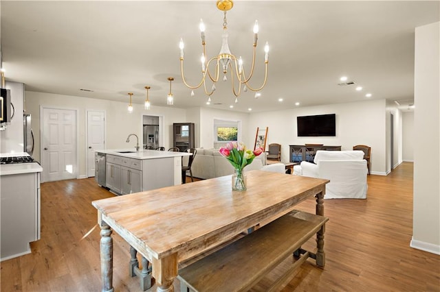 dining space with sink, light hardwood / wood-style floors, and an inviting chandelier