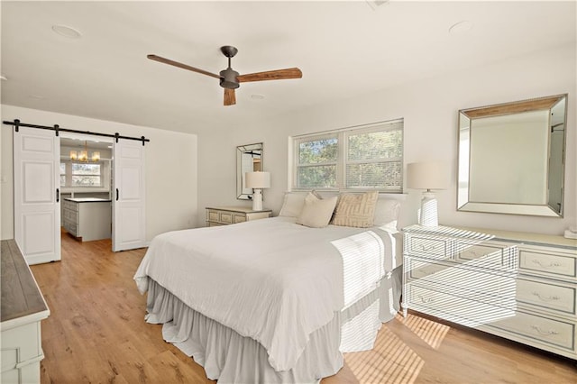 bedroom with light wood-type flooring, a barn door, and ceiling fan