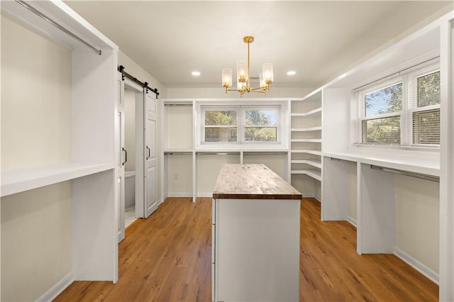 spacious closet with a barn door, light hardwood / wood-style floors, and an inviting chandelier