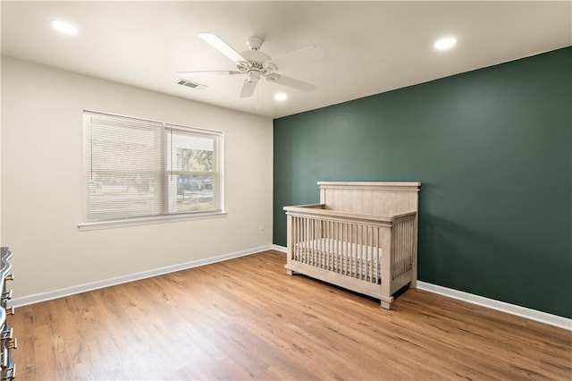 bedroom with a crib, light wood-type flooring, and ceiling fan