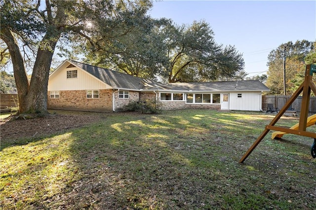 rear view of property featuring a playground and a lawn