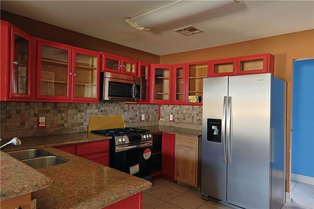 kitchen featuring tasteful backsplash, stainless steel appliances, sink, light tile patterned floors, and dark stone countertops