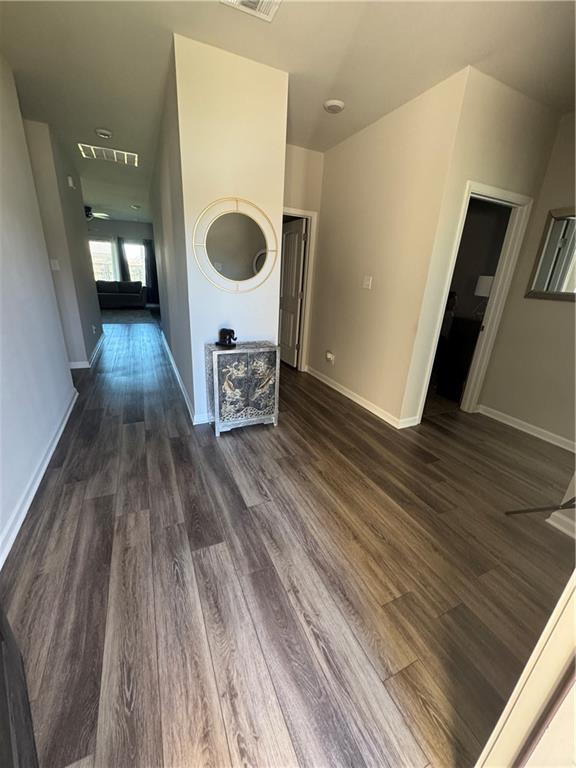 hall with dark wood finished floors, visible vents, and baseboards