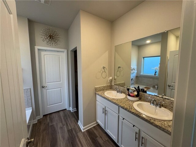 full bath with a sink, wood finished floors, double vanity, and a bath