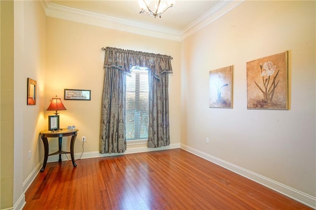 empty room featuring crown molding, wood-type flooring, and an inviting chandelier