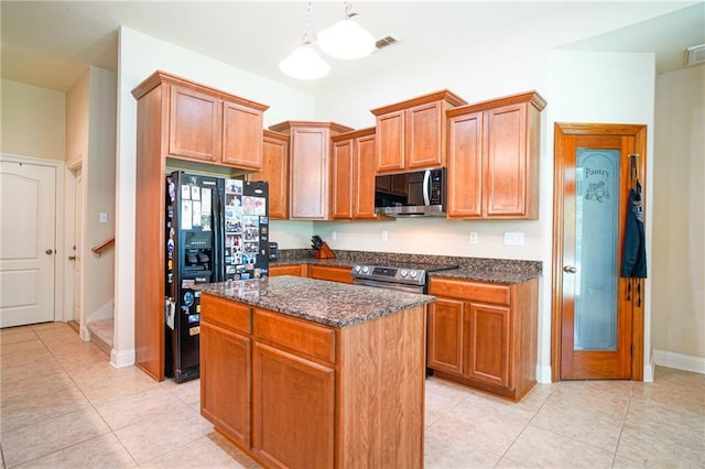 kitchen featuring appliances with stainless steel finishes, light tile patterned floors, pendant lighting, dark stone countertops, and a center island