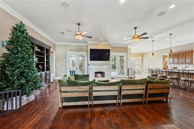 living room with dark hardwood / wood-style flooring, ornamental molding, a premium fireplace, and ceiling fan with notable chandelier