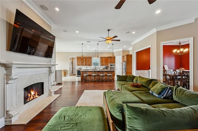 living room featuring a premium fireplace, crown molding, dark hardwood / wood-style flooring, and ceiling fan with notable chandelier