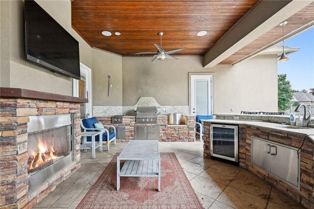 view of patio / terrace featuring exterior kitchen, an outdoor stone fireplace, a grill, sink, and wine cooler