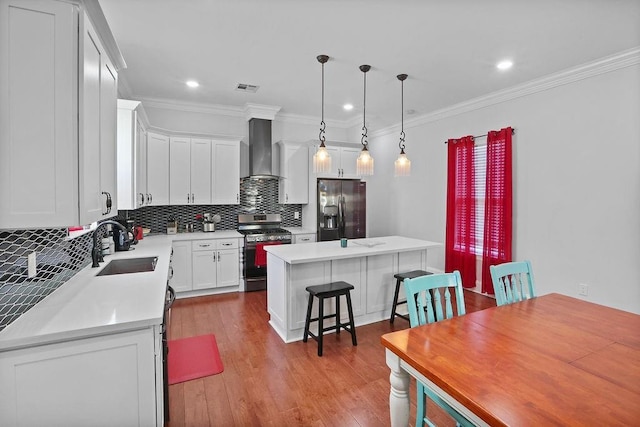 kitchen with wall chimney exhaust hood, stainless steel appliances, pendant lighting, white cabinetry, and a kitchen island