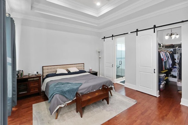 bedroom with a barn door, dark hardwood / wood-style flooring, crown molding, a walk in closet, and a closet