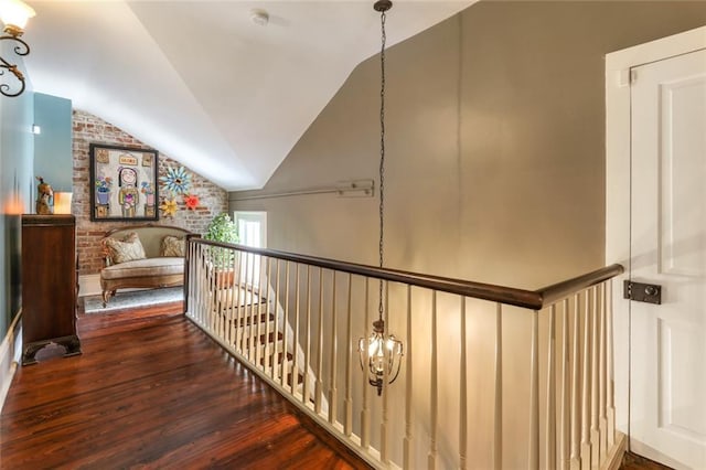 hallway featuring brick wall, dark wood-type flooring, lofted ceiling, and a notable chandelier