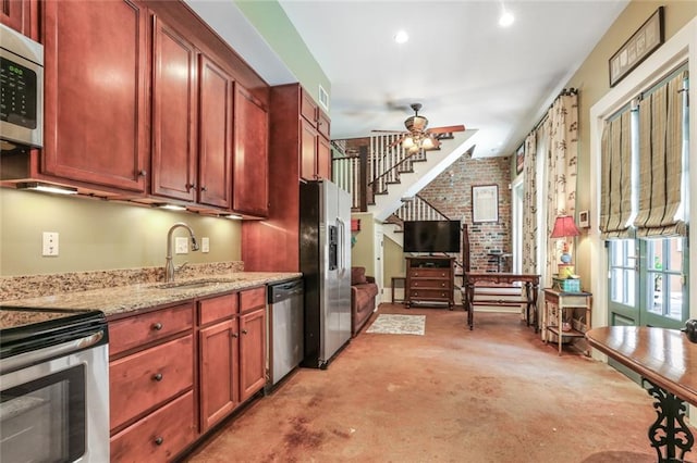 kitchen with light stone countertops, appliances with stainless steel finishes, brick wall, ceiling fan, and sink