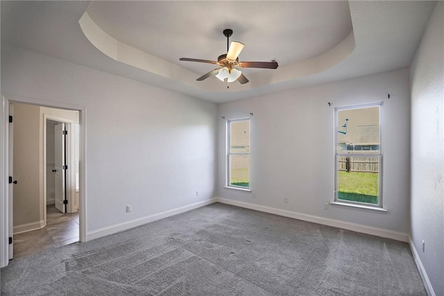 carpeted empty room featuring a raised ceiling, a wealth of natural light, and ceiling fan