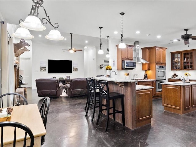 kitchen featuring pendant lighting, wall chimney range hood, appliances with stainless steel finishes, a kitchen bar, and kitchen peninsula