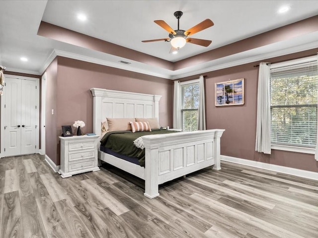 bedroom with light hardwood / wood-style floors, a raised ceiling, ceiling fan, and crown molding