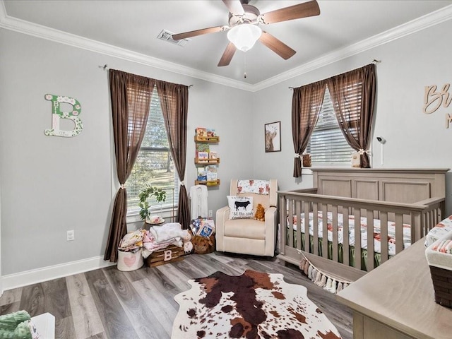 bedroom featuring multiple windows, ceiling fan, hardwood / wood-style floors, and a nursery area