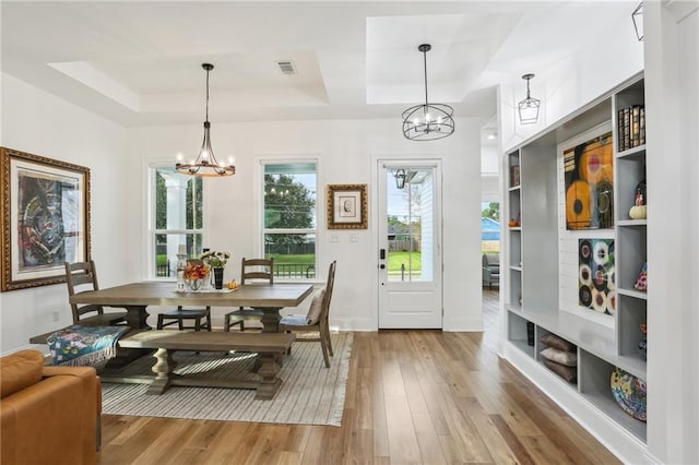 dining area with a tray ceiling, a notable chandelier, and light wood-type flooring