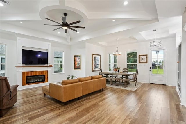 living room with ceiling fan with notable chandelier, light hardwood / wood-style floors, and a tray ceiling