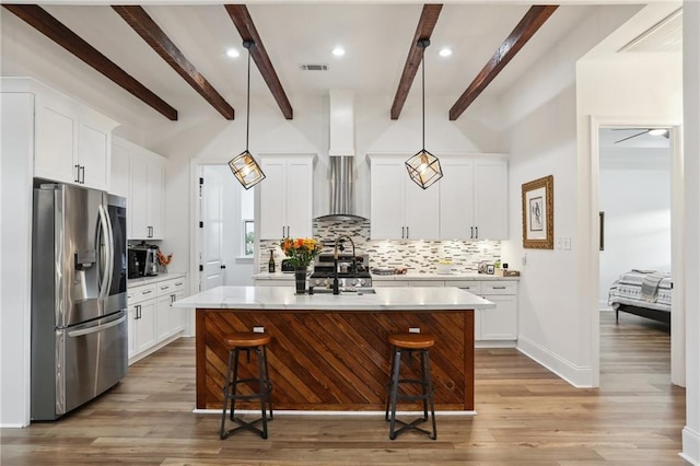 kitchen with a kitchen breakfast bar, a kitchen island with sink, white cabinets, stainless steel fridge with ice dispenser, and hanging light fixtures