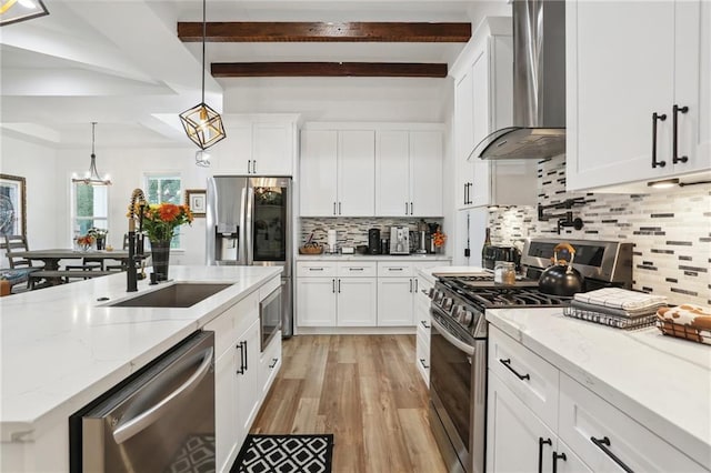 kitchen featuring decorative backsplash, appliances with stainless steel finishes, wall chimney exhaust hood, white cabinetry, and hanging light fixtures