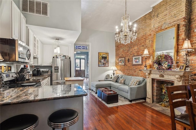 kitchen with white cabinets, dark hardwood / wood-style floors, kitchen peninsula, stainless steel appliances, and brick wall